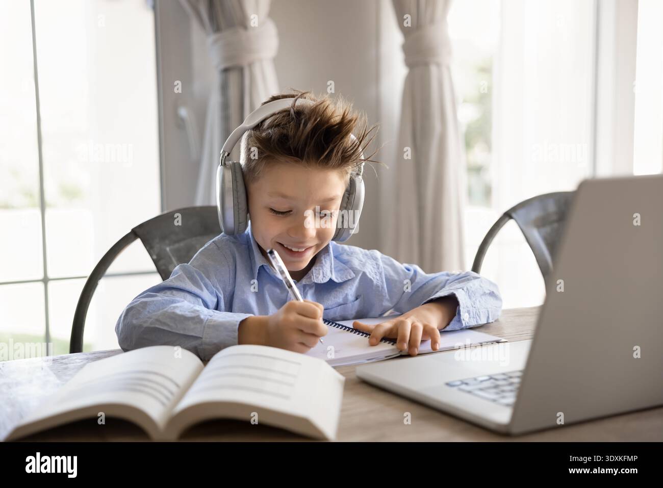 Smiling school boy studying remotely sit at table with laptop Stock Photo