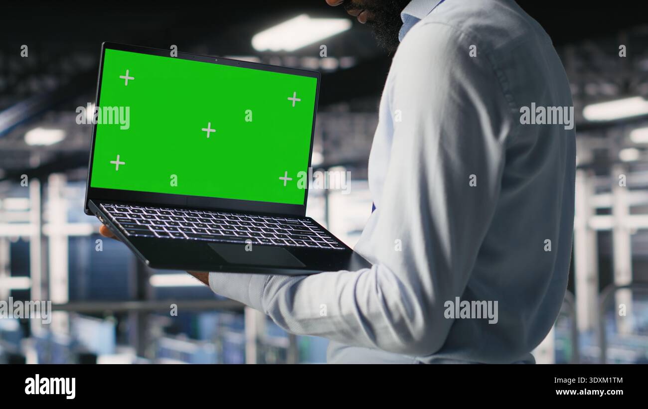 Technicians on data center industrial platform analyzing performance outputs on green screen laptop. Server hub engineering team finetuning server rig configurations using mockup notebook Stock Photo