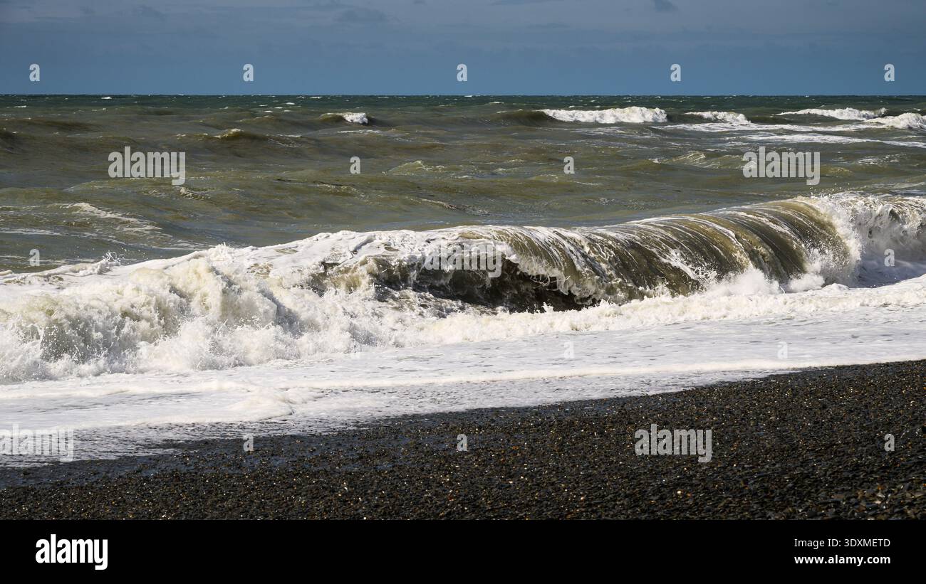 Angry storm waves roll ashore on stone beach creating surf Stock Photo