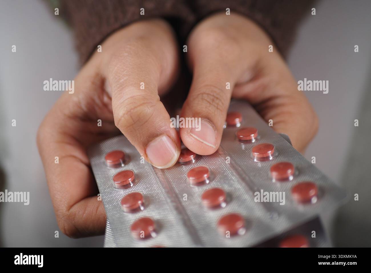 Hands hold a blister pack of red pills in a simple setting Stock Photo