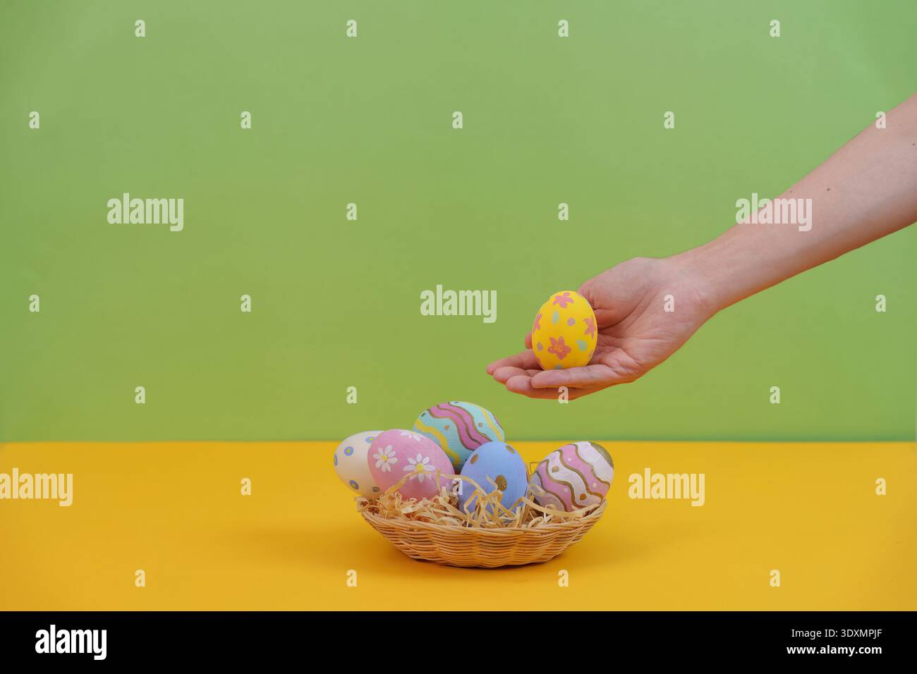 SSTK Easter. Hand holding yellow Easter egg above colorful basket. Stock Photo