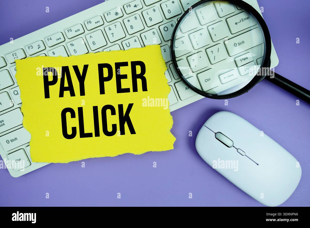 Yellow torn paper with the text "Pay Per Click" placed on a white keyboard, and magnifying glass and a computer mouse Stock Photo