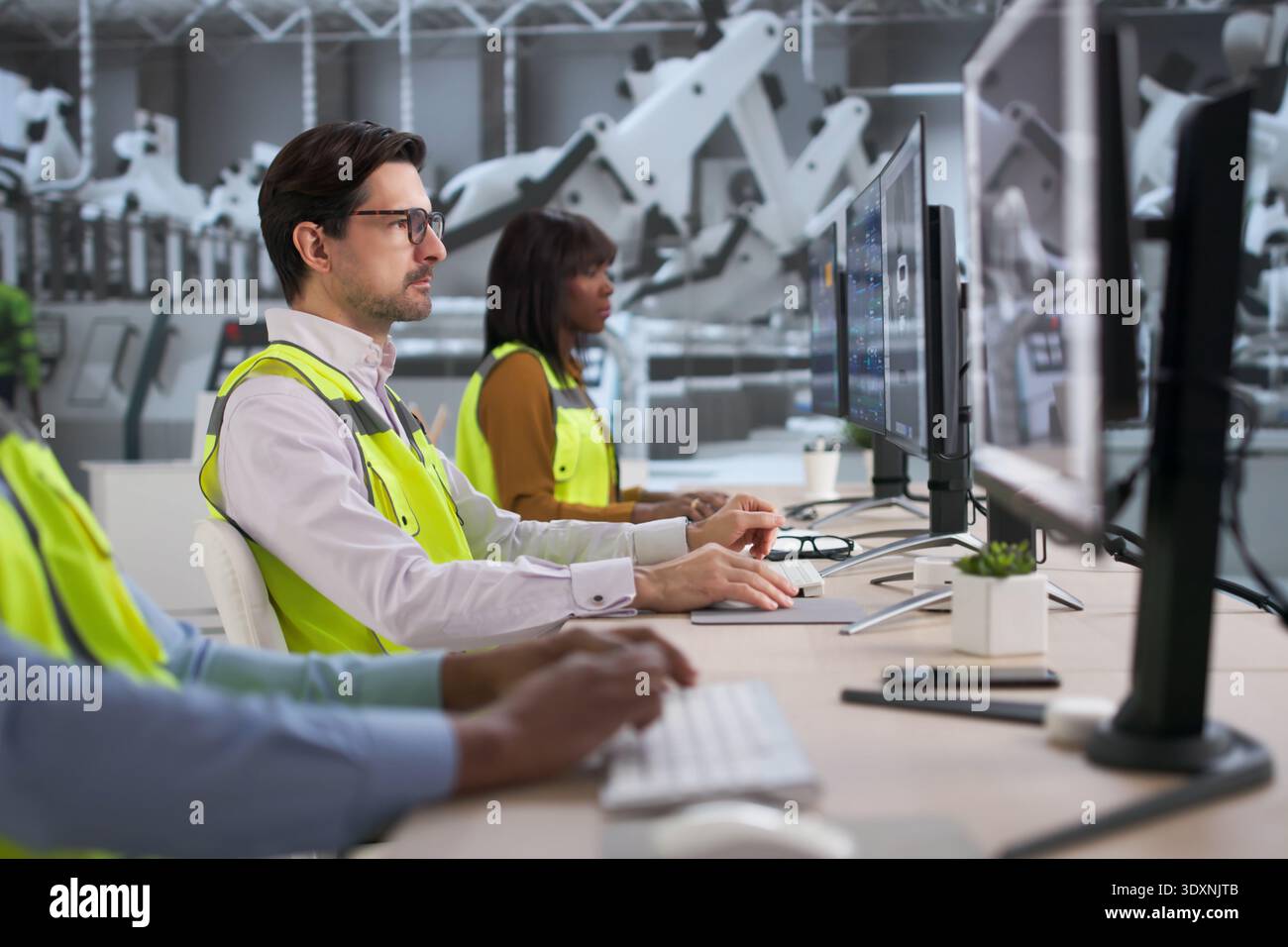 Diverse Team Of Engineers And Technicians Using Computers Near Car Assembly Line. Young Software Developers Stock Photo