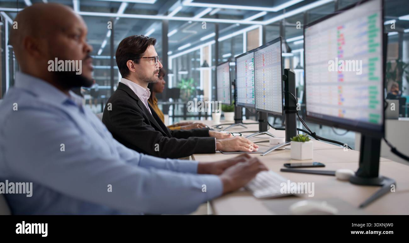 Diverse Team Studies Bills And Data On Computers In Office Setting. People Working With Spreadsheets And Documents Stock Photo