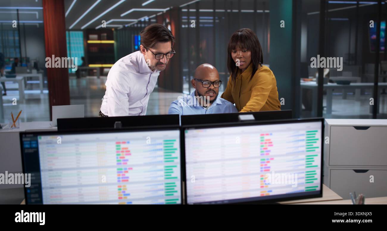 Diverse Team Meets In Office, Analyzing Data On Computers And Spreadsheets. A Professional Coder Works Stock Photo
