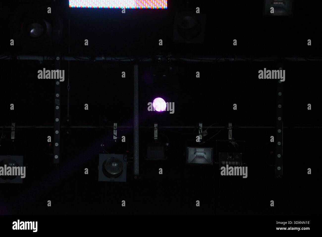 Professional stage lighting rig with purple spotlight and LED panels mounted on a dark ceiling. Modern lighting equipment creates dramatic atmosphere Stock Photo