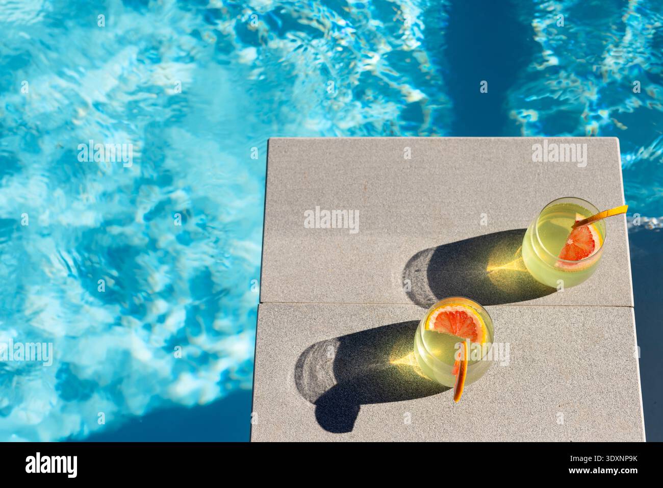 Two stemless glasses sitting on concrete pool coping, casting long shadows and rippling reflections Stock Photo
