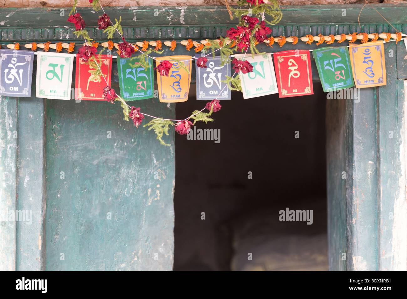 Buddhist prayer flags and floral garlands at the entrance of a traditional Gurung house in Ghandruk, Nepal. Stock Photo