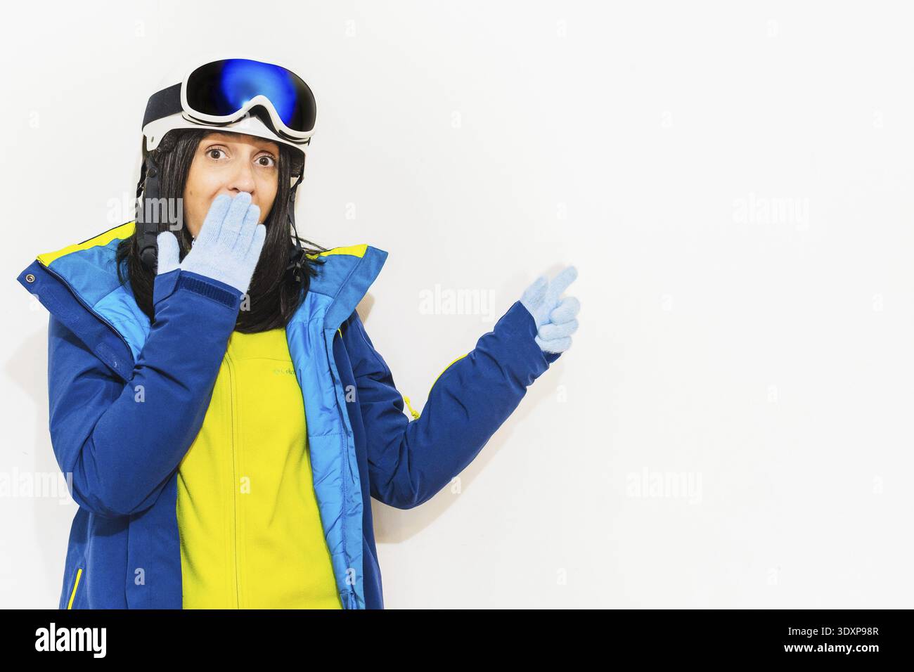 Skier young woman wearing warm padded windbreaker jacket hat ski goggles mask point index finger aside on copy space blank area travel rest spend week Stock Photo