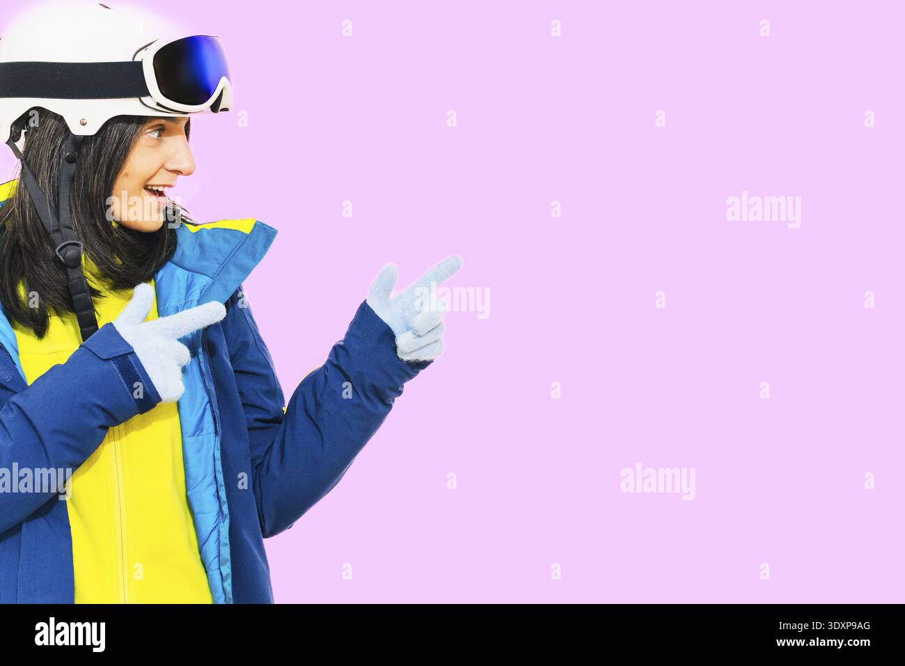 Skier young woman wearing warm padded windbreaker jacket hat ski goggles mask point index finger aside on copy space blank area travel rest spend week Stock Photo