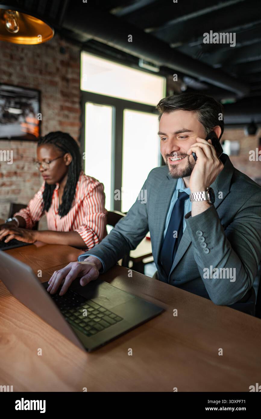 Businessman talking on smartphone while working on laptop Stock Photo