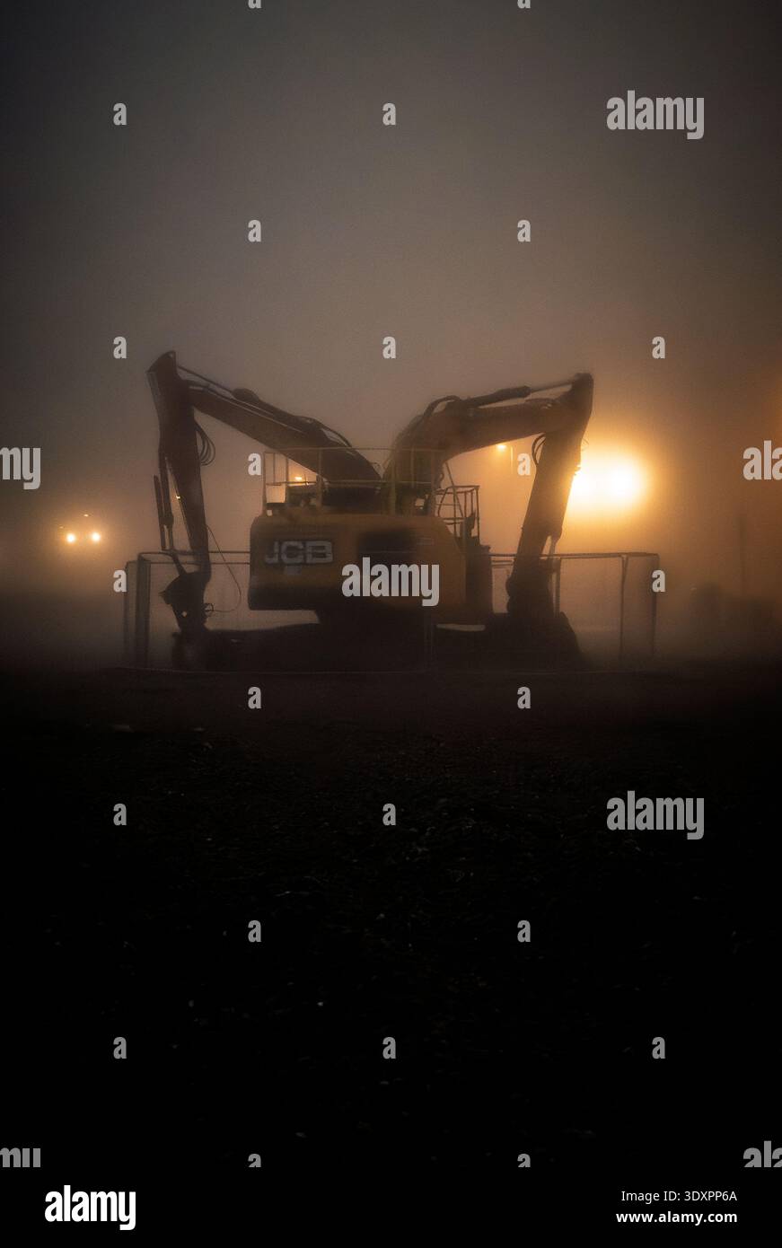 Atmospheric foggy night view of JCB excavator working on coastal protection works at Worthing beach in West Sussex, silhouetted heavy machinery - Smartphone Captured Stock Image