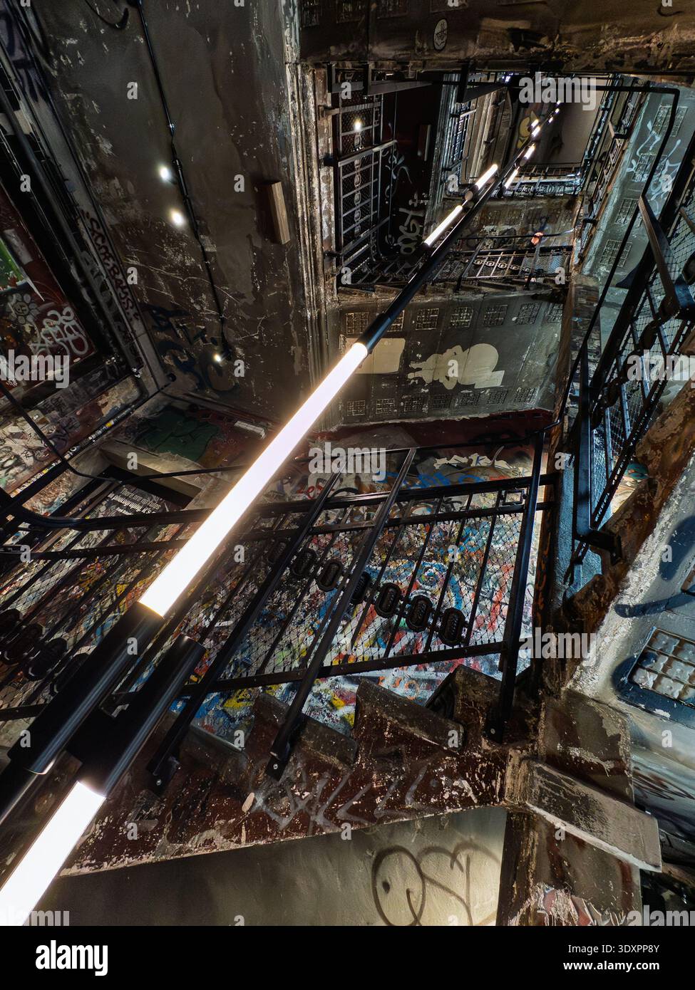 Dramatic low-angle view of graffiti-covered stairwell in Fotografiska Berlin museum, former Kunsthaus Tacheles art squat in Mitte with neon LED lights - Smartphone Captured Stock Image