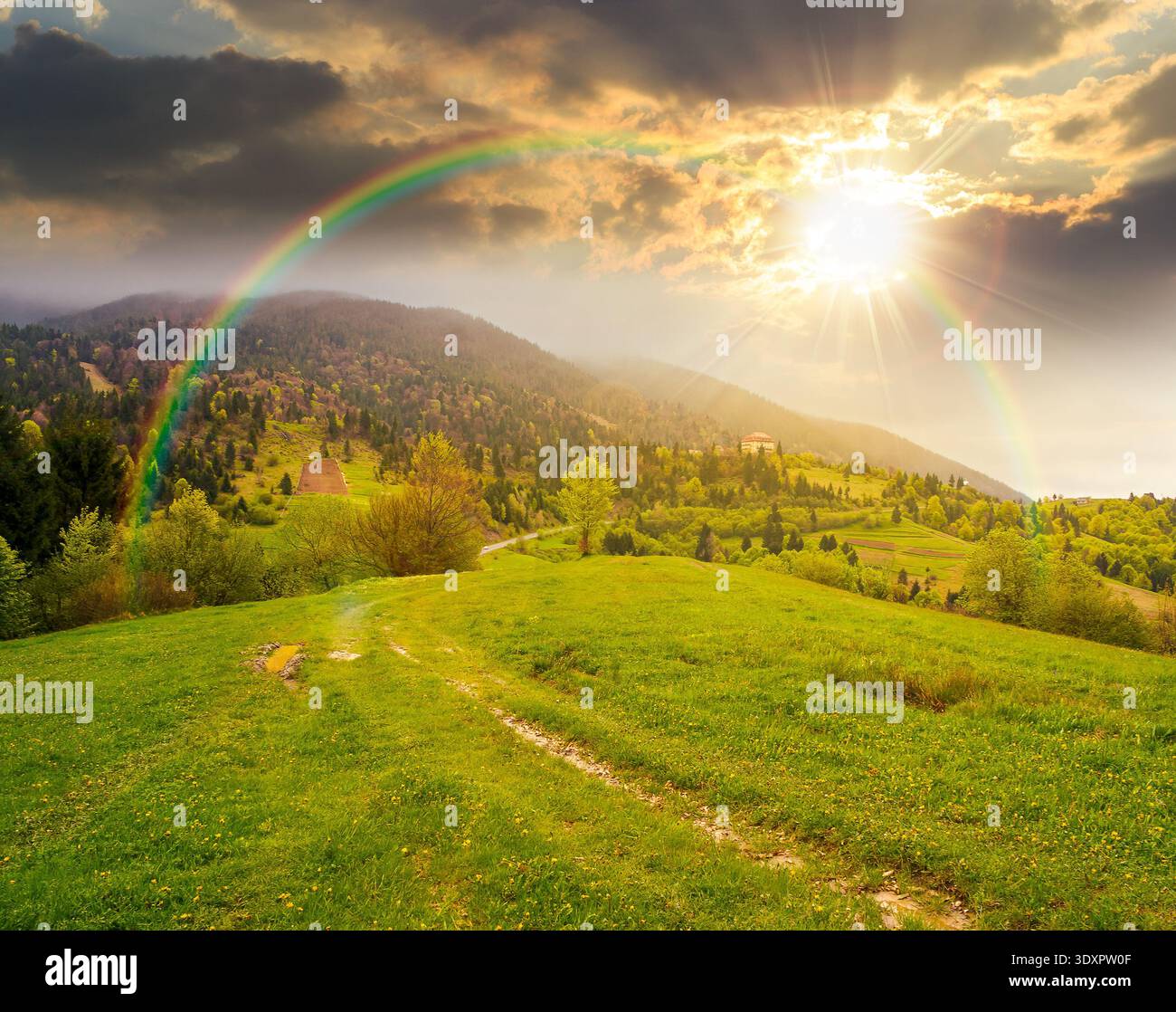 remote countryside in mountain landscape at sunset. hazy weather during spring in evening light. dirt road through lush green pasture on a hill. alpin Stock Photo