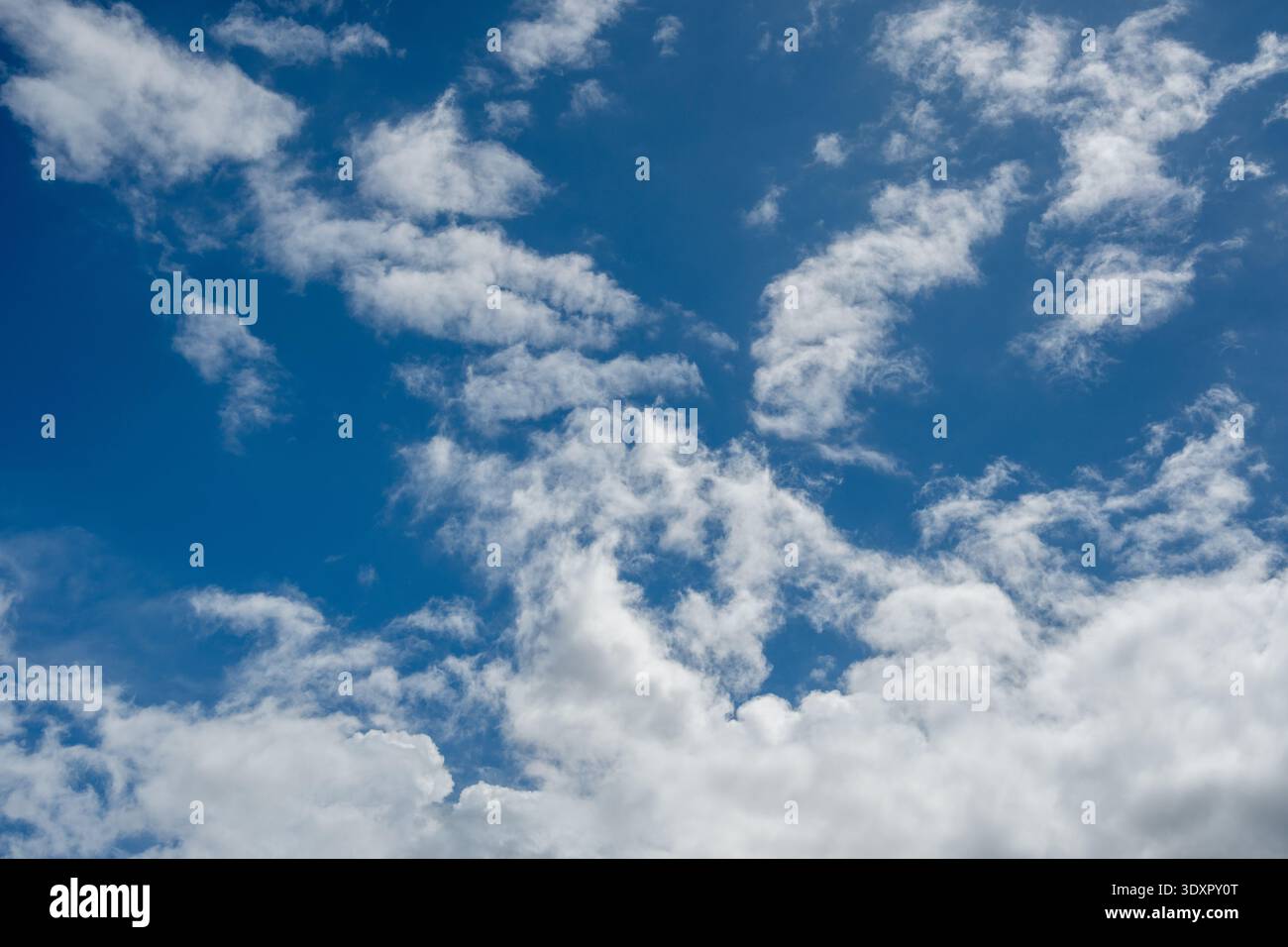 Dispersed white clouds floating against a solid blue sky Stock Photo