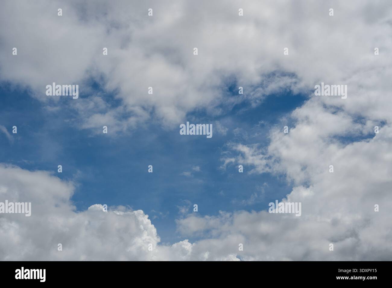 Blue sky visible through an opening in thick white clouds Stock Photo