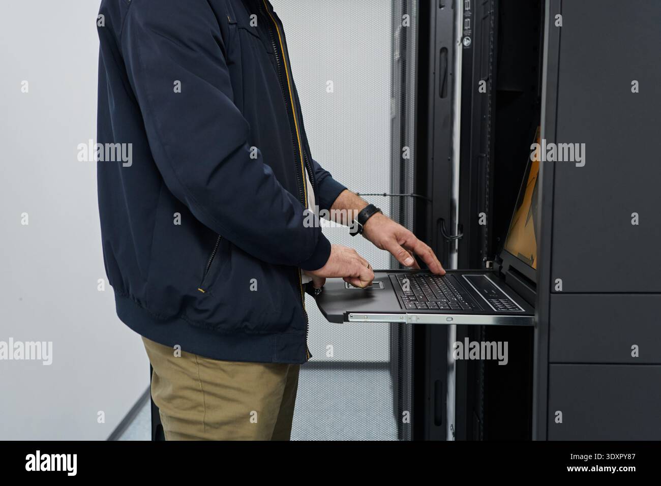 IT technician working on laptop in server rack inside data center performing network maintenance and hardware monitoring Stock Photo