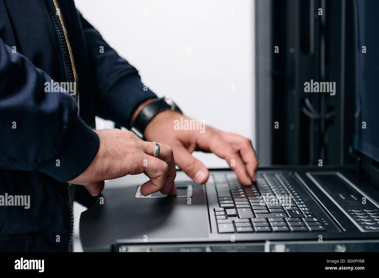 IT technician typing on laptop console in a data center server rack performing maintenance Stock Photo