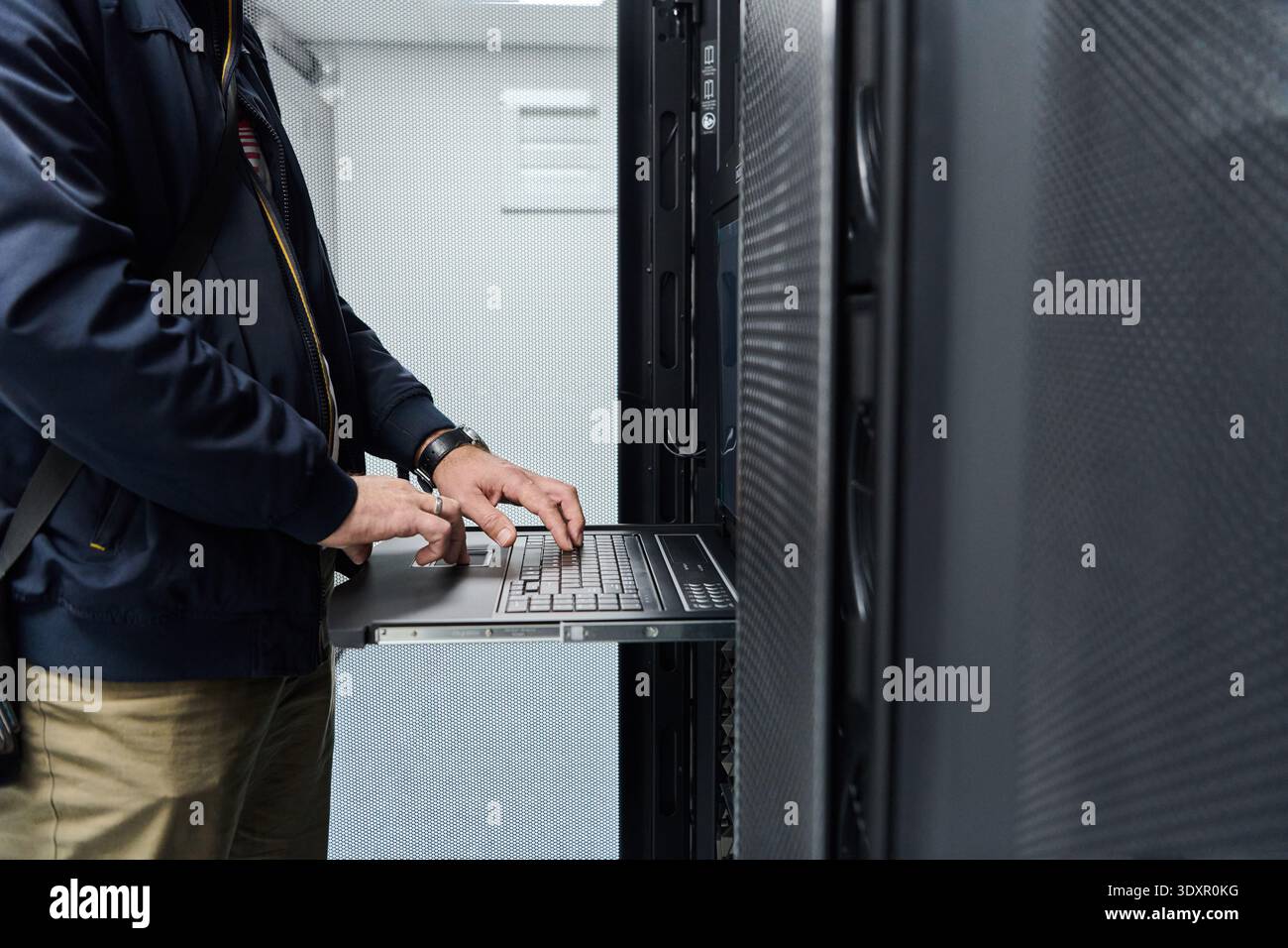 IT technician using rack console laptop to service servers in a data center server room Stock Photo