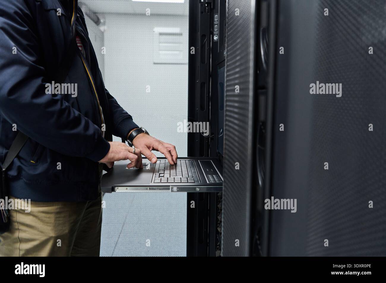 IT technician maintaining server rack with pull-out console laptop in a data center Stock Photo