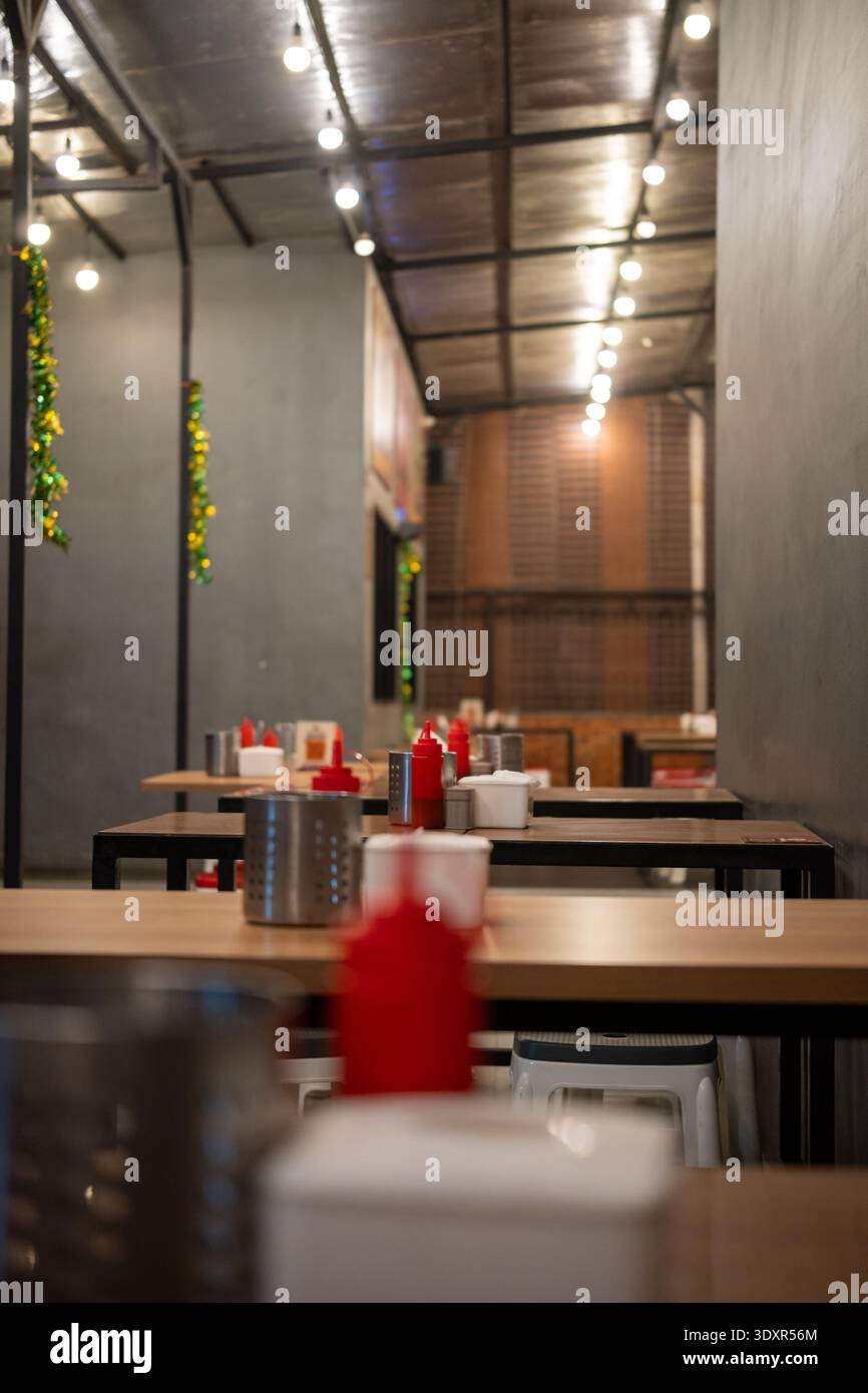 Empty wooden tables with red squeeze bottles under string lights Stock Photo
