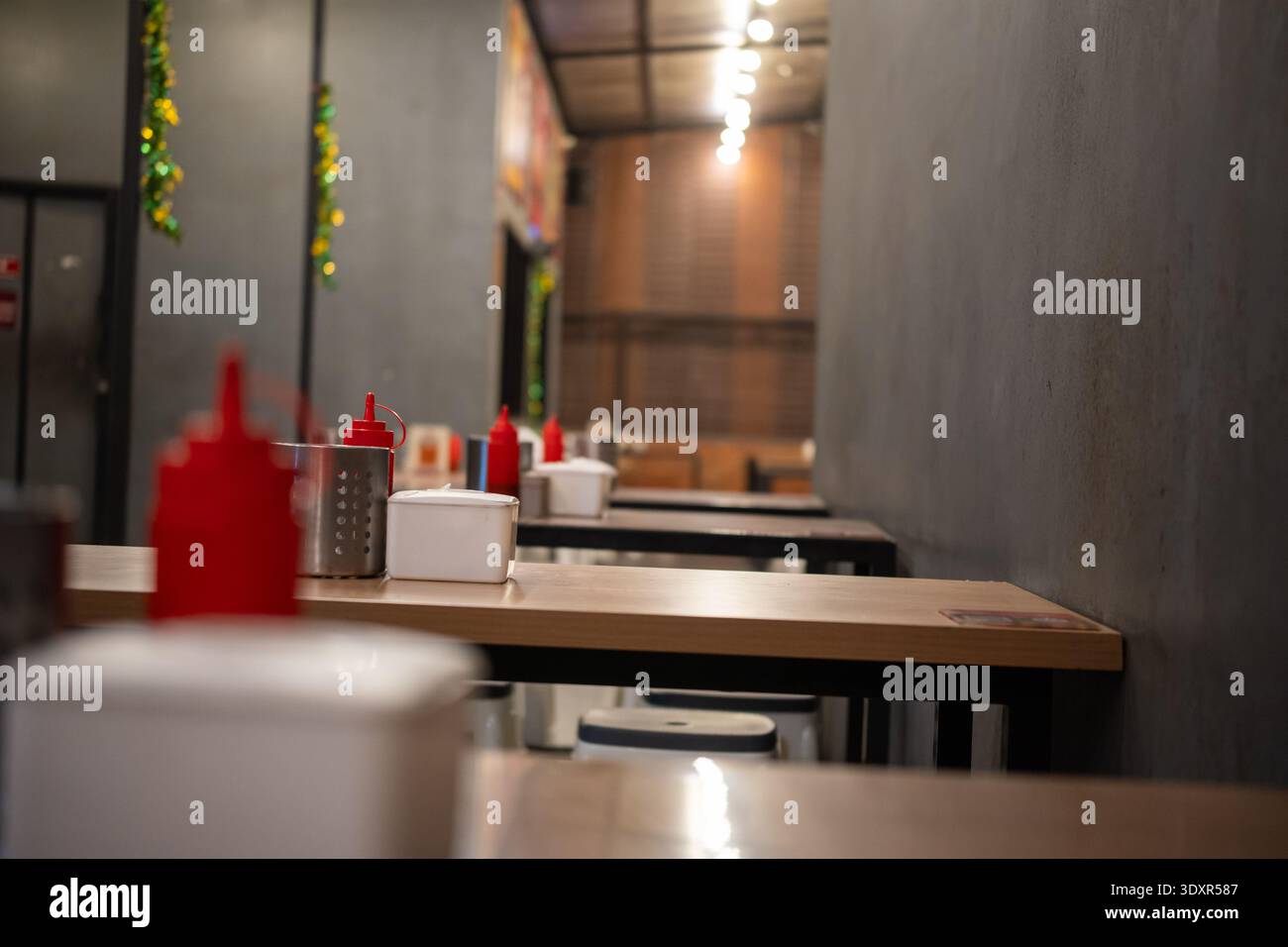 Empty wooden tables with red squeeze bottles in a dim indoor space Stock Photo