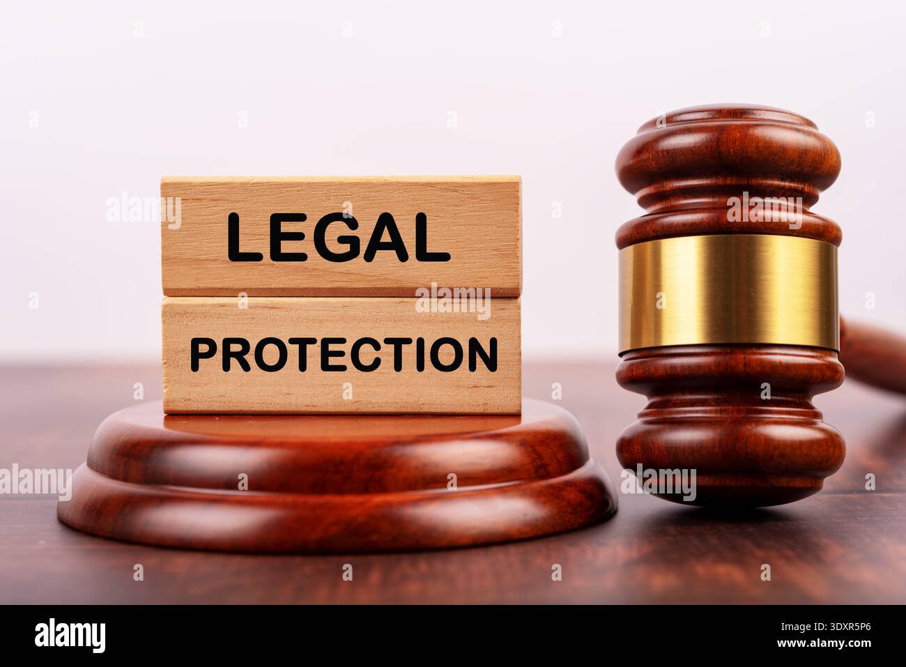 Wooden blocks with 'LEGAL PROTECTION' text placed on a judge's gavel sound block, symbolizing law and rights. Stock Photo