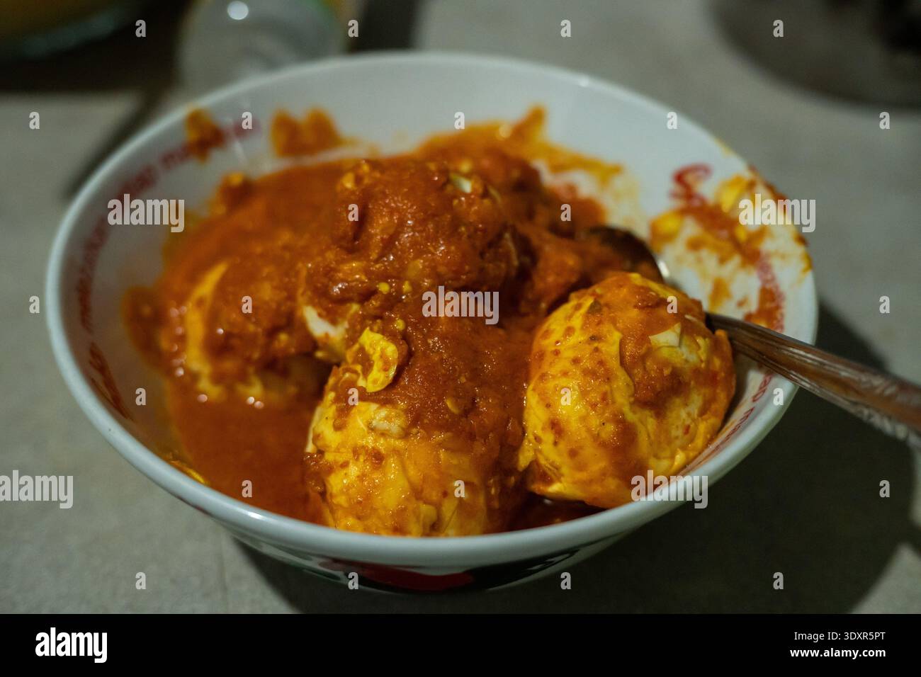 Boiled eggs covered in red chili sauce in a white bowl Stock Photo