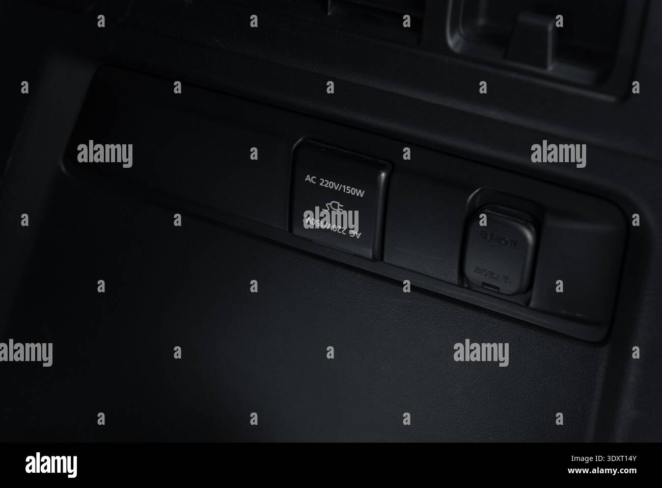 Electrical power outlets in car trunk. Close-up view of a AC 220V power socket with an open cover and a 12V auxiliary power outlet on a dark plastic. Stock Photo