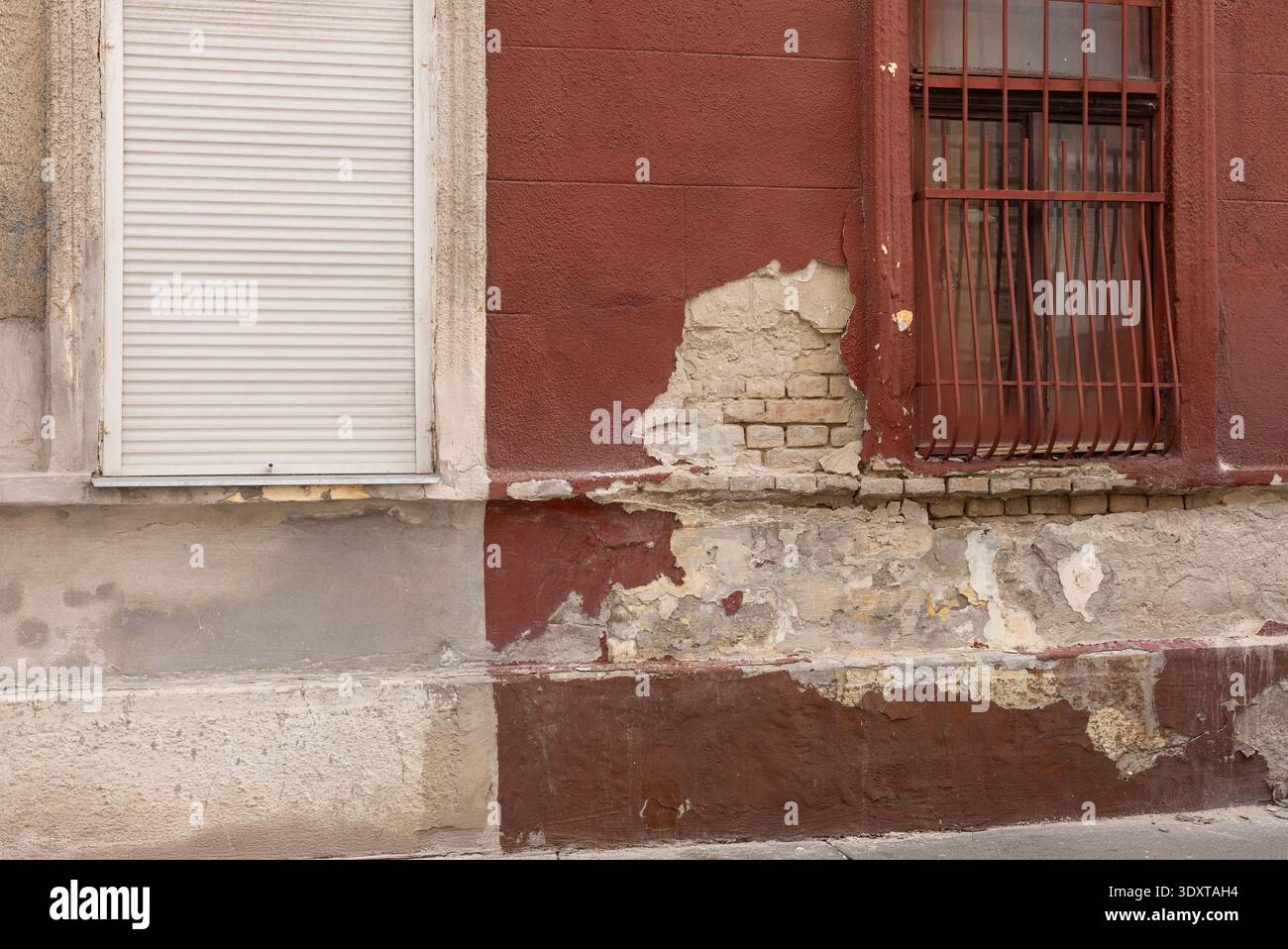 Distressed red facade with peeling plaster and iron security bars on window. Stock Photo