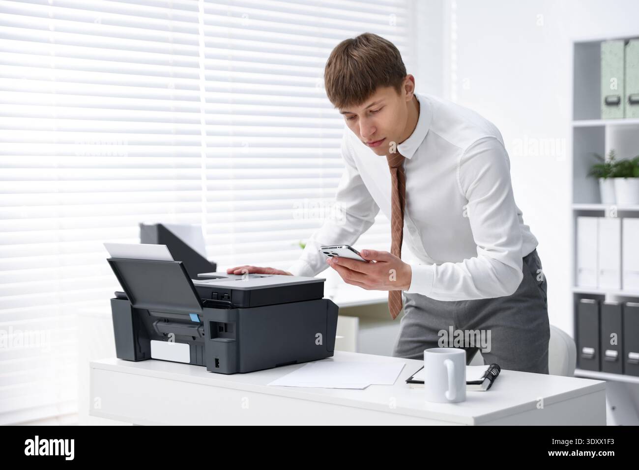 Man using printer and smartphone at white desk in office Stock Photo