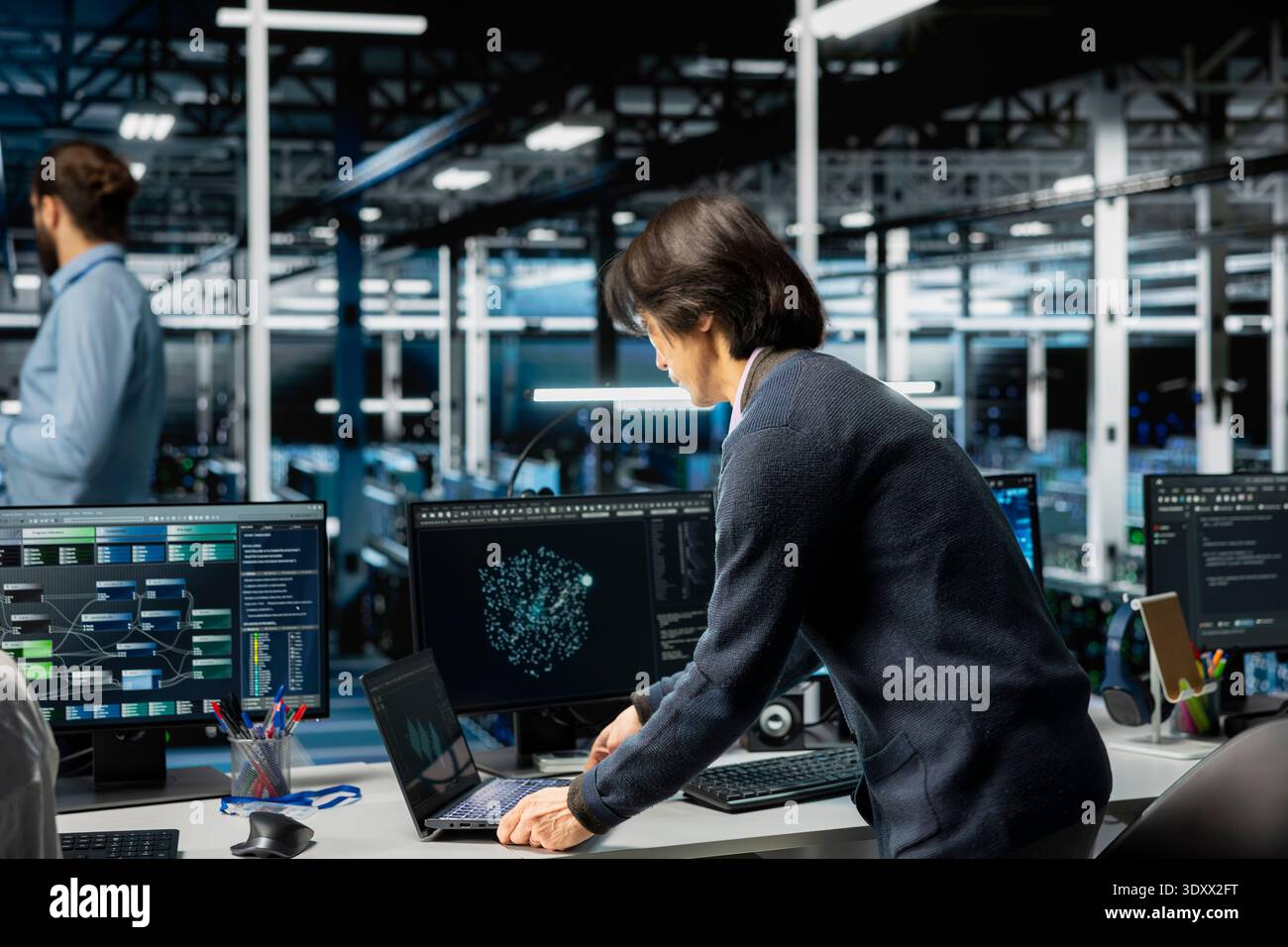 Software developer in server room office using device to review infrastructure diagnostics. Man in high tech data center analyzing performance data to maintain system uptime Stock Photo