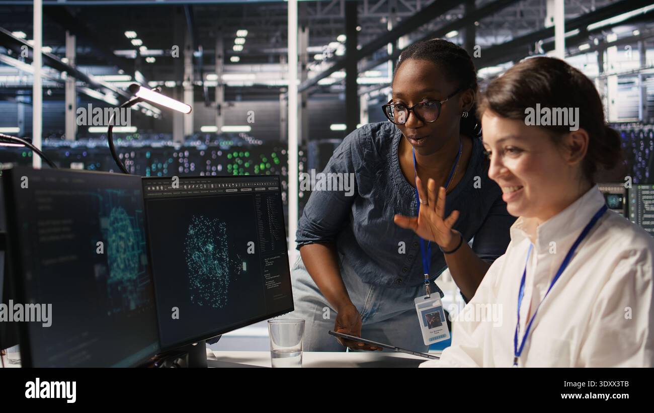 Cheerful data center engineers doing fist bump after completing successful AI system deployment. Smiling coworkers celebrating after achieving optimal machine learning model performance, camera A Stock Photo