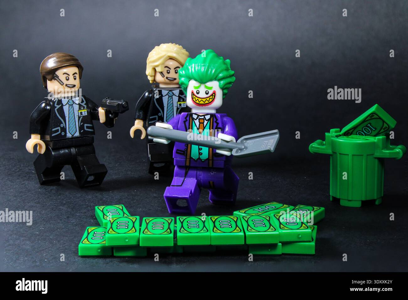 Lego Joker robbing a bank holding a shovel and stacks of money being surrounded by officers pointing a gun at him Stock Photo
