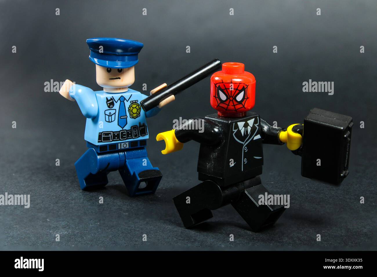 Lego Spiderman minifigure with a briefcase being chased by a police officer holding a stick in his hands Stock Photo