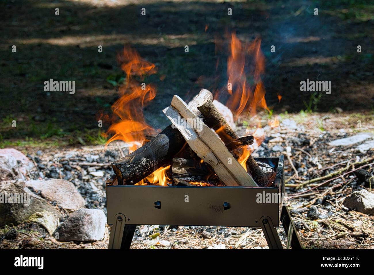 A daytime campfire blazes in a portable metal fire pit with stacked ...