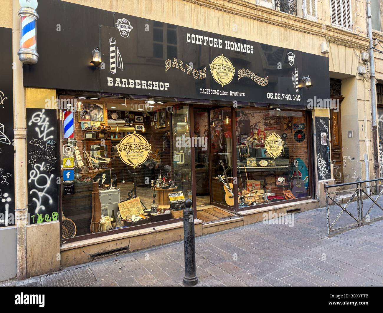 Dalton Brothers Barbershop. Marseille, France. Vintage signage and display window featuring retro items, barber pole, guitars. Stock Photo