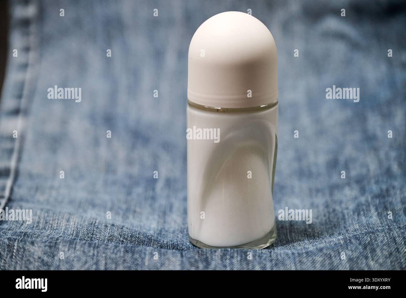 A small glass bottle of deodorant on a blue jeans denim background Stock Photo