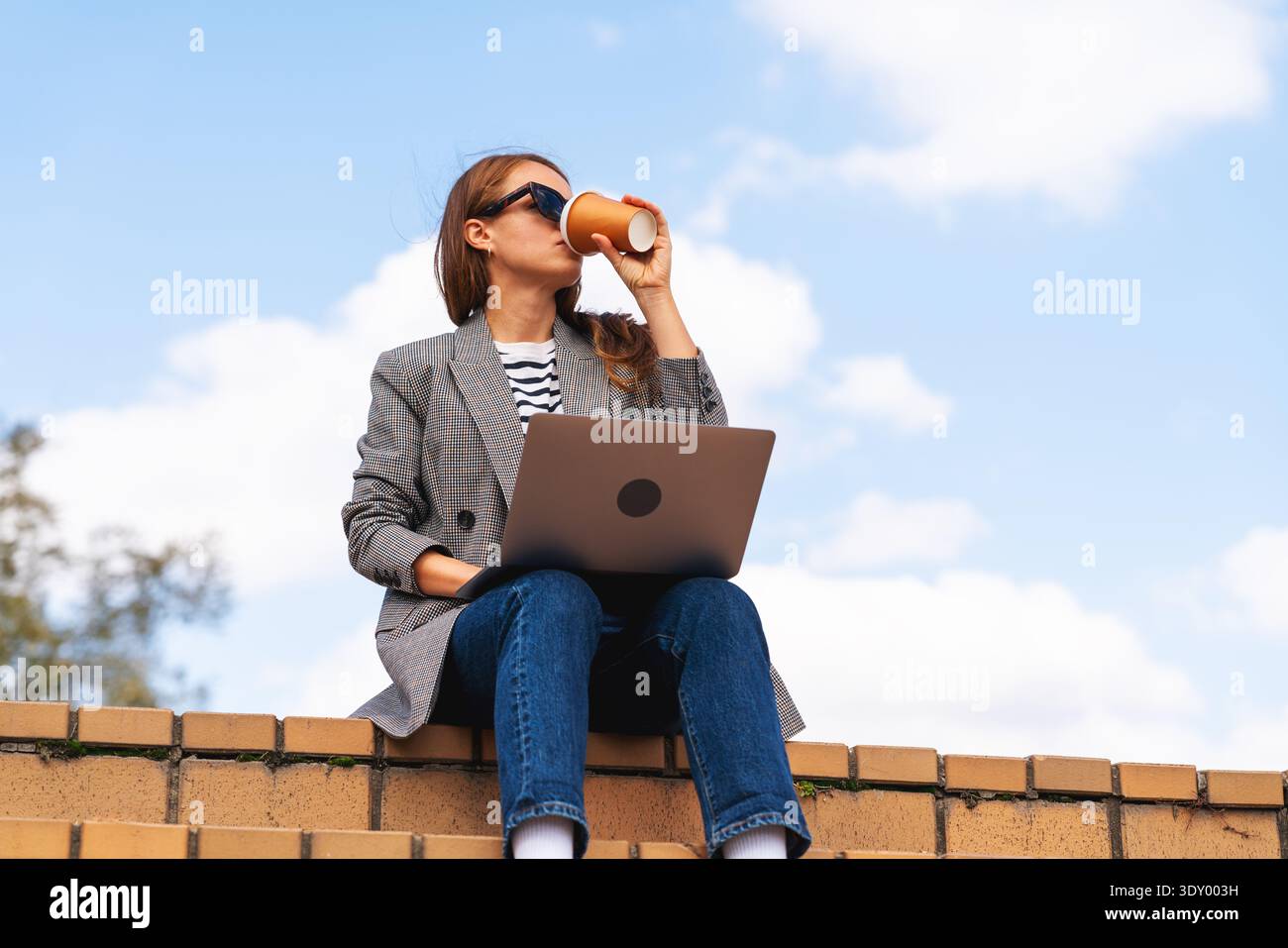 Young professional drinking coffee while working remotely on city steps. Stock Photo