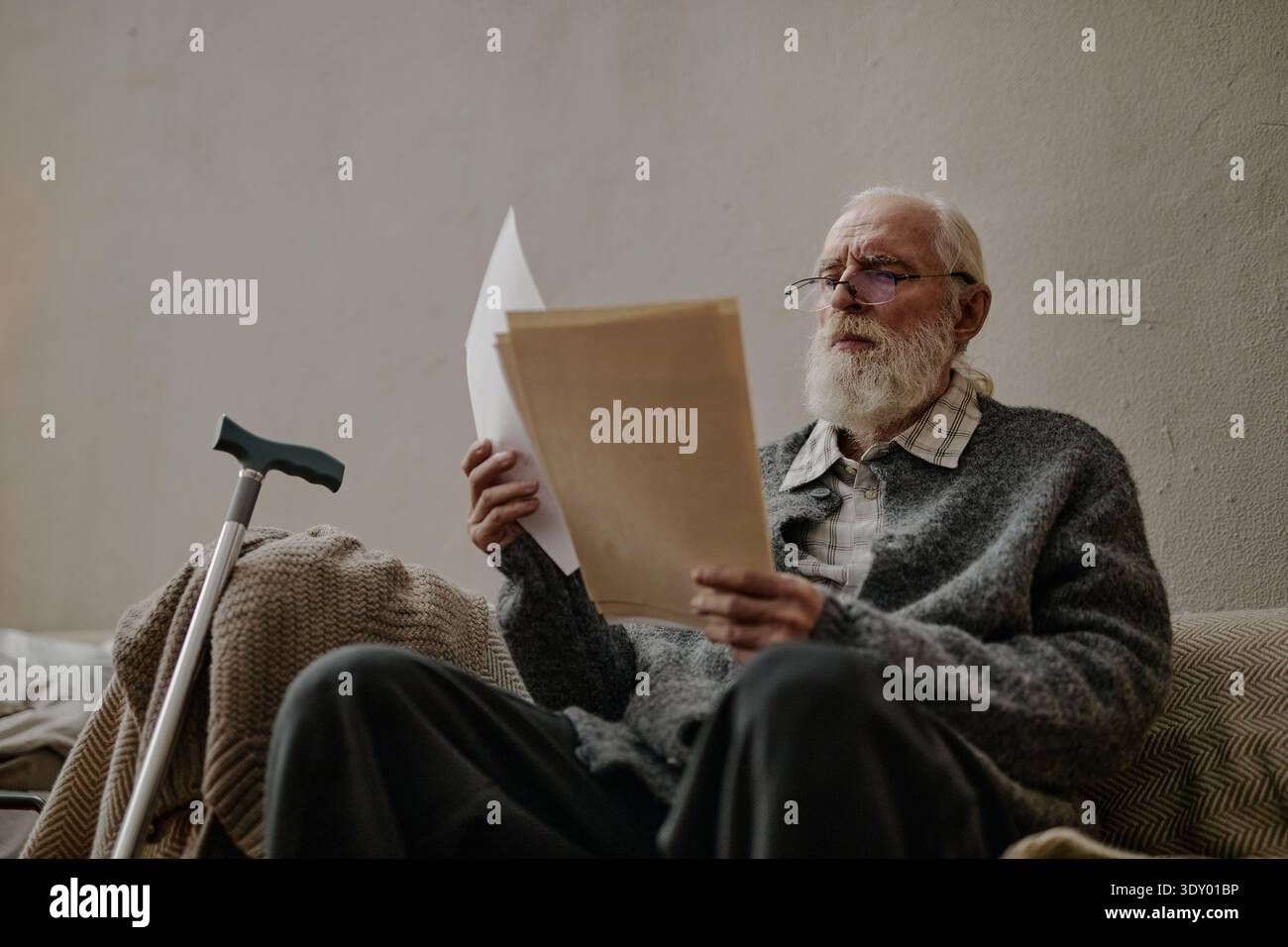 Senior Caucasian Man Reading Documents While Sitting Beside Walking Cane Stock Photo