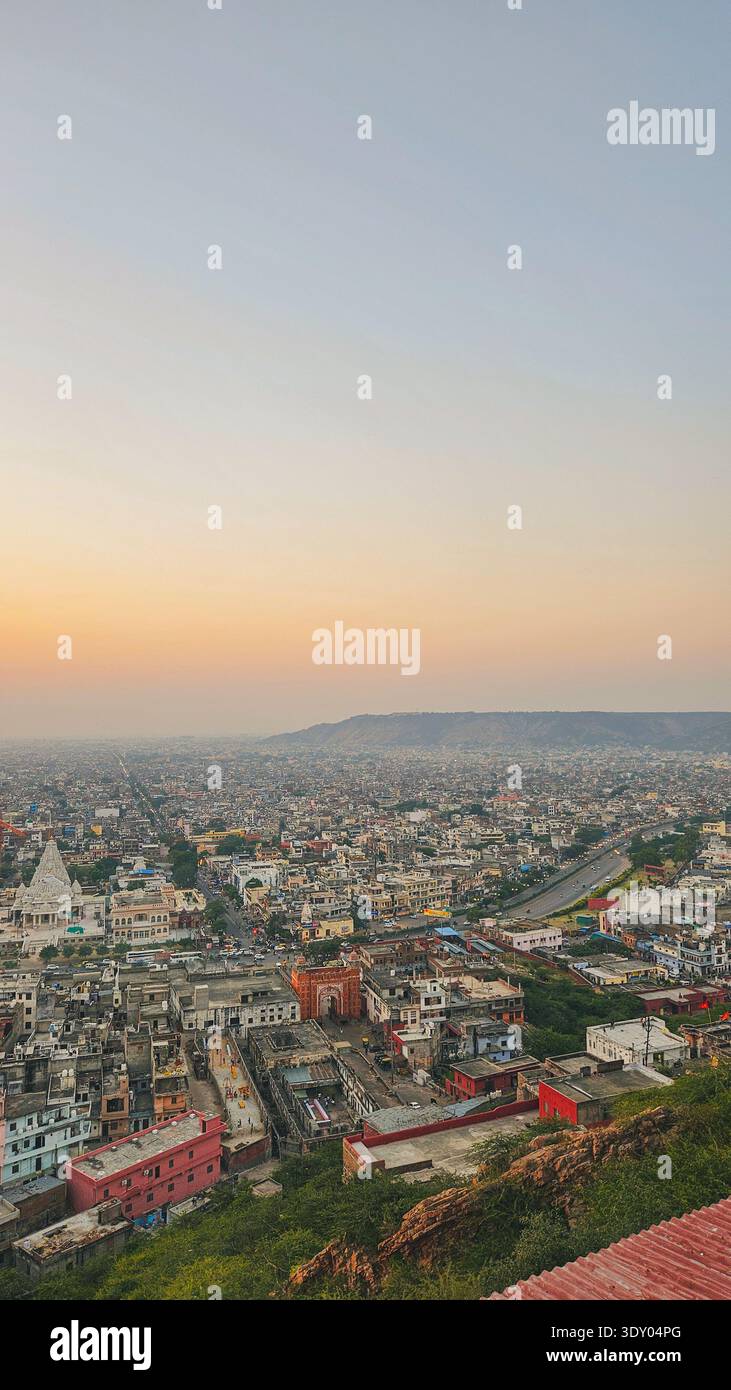 Panoramic view of a densely built cityscape at sunset, seen from a hilltop with warm orange hues spreading across the sky. - Smartphone Captured Stock Image
