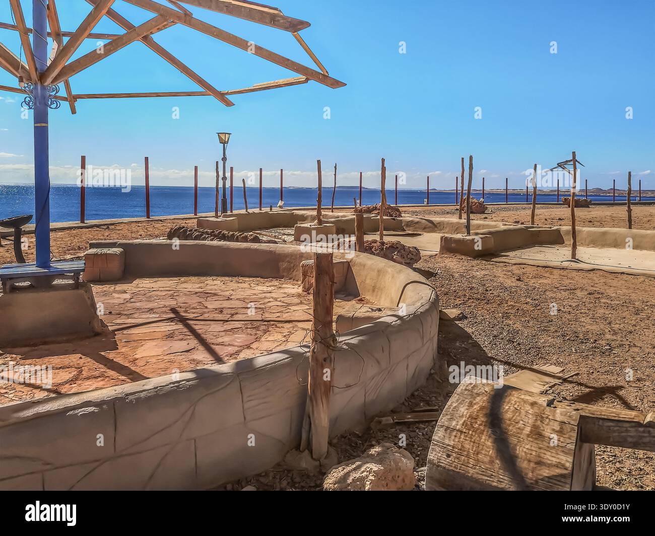Dry wooden poles stick out of the sand on an abandoned beach in Sharm El Sheikh, Egypt. Many pillars against the background of the blue water - Smartphone Captured Stock Image