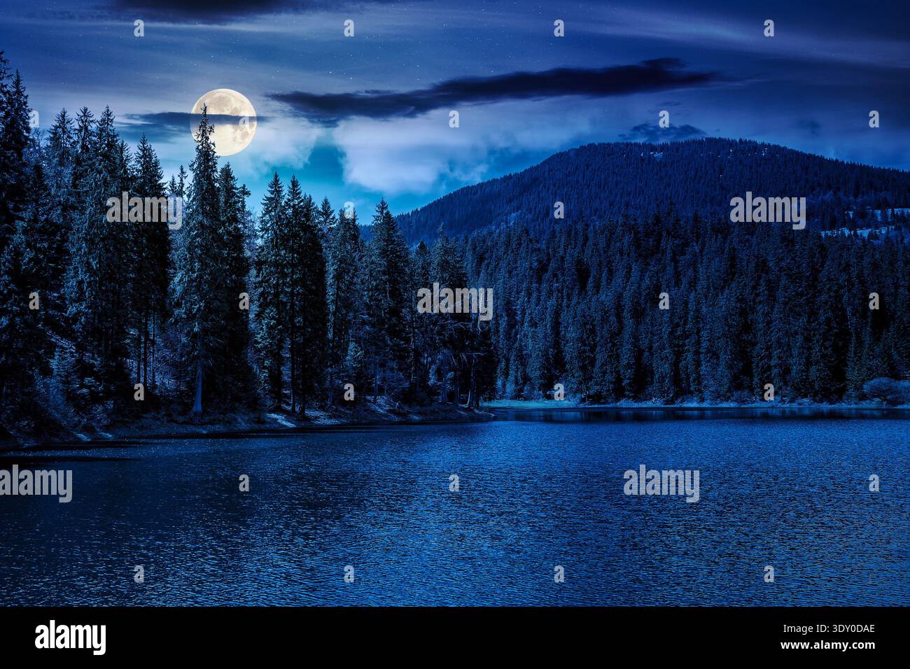 mountain lake among the green spruce forest in beautiful spring landscape at night. moon over rippled water surface. mysterious alpine nature scenery Stock Photo