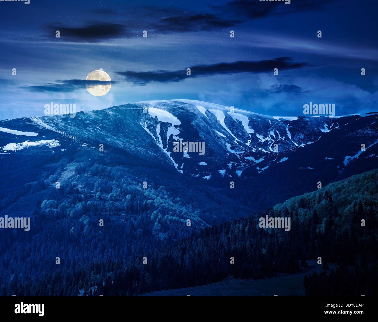mysterious nature image of ridge with snow capped tops in spring landscape. mountain background wallpaper at night. full moon over greenery scenery wi Stock Photo