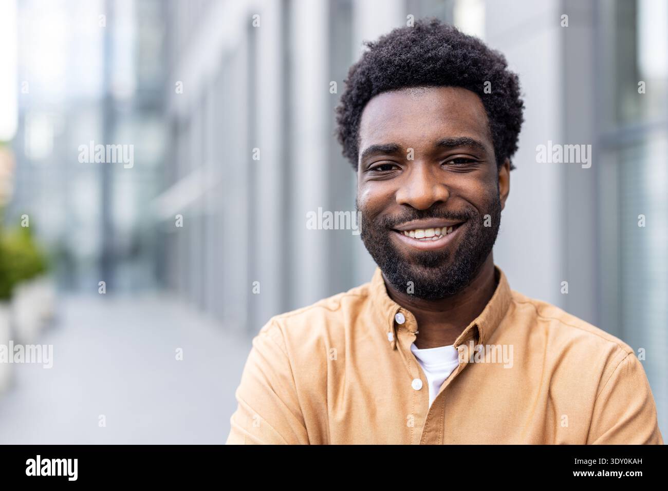 Confident young african person smiling brightly while standing outdoors in a city environment, expressing happiness and success with a friendly, welcoming demeanor Stock Photo
