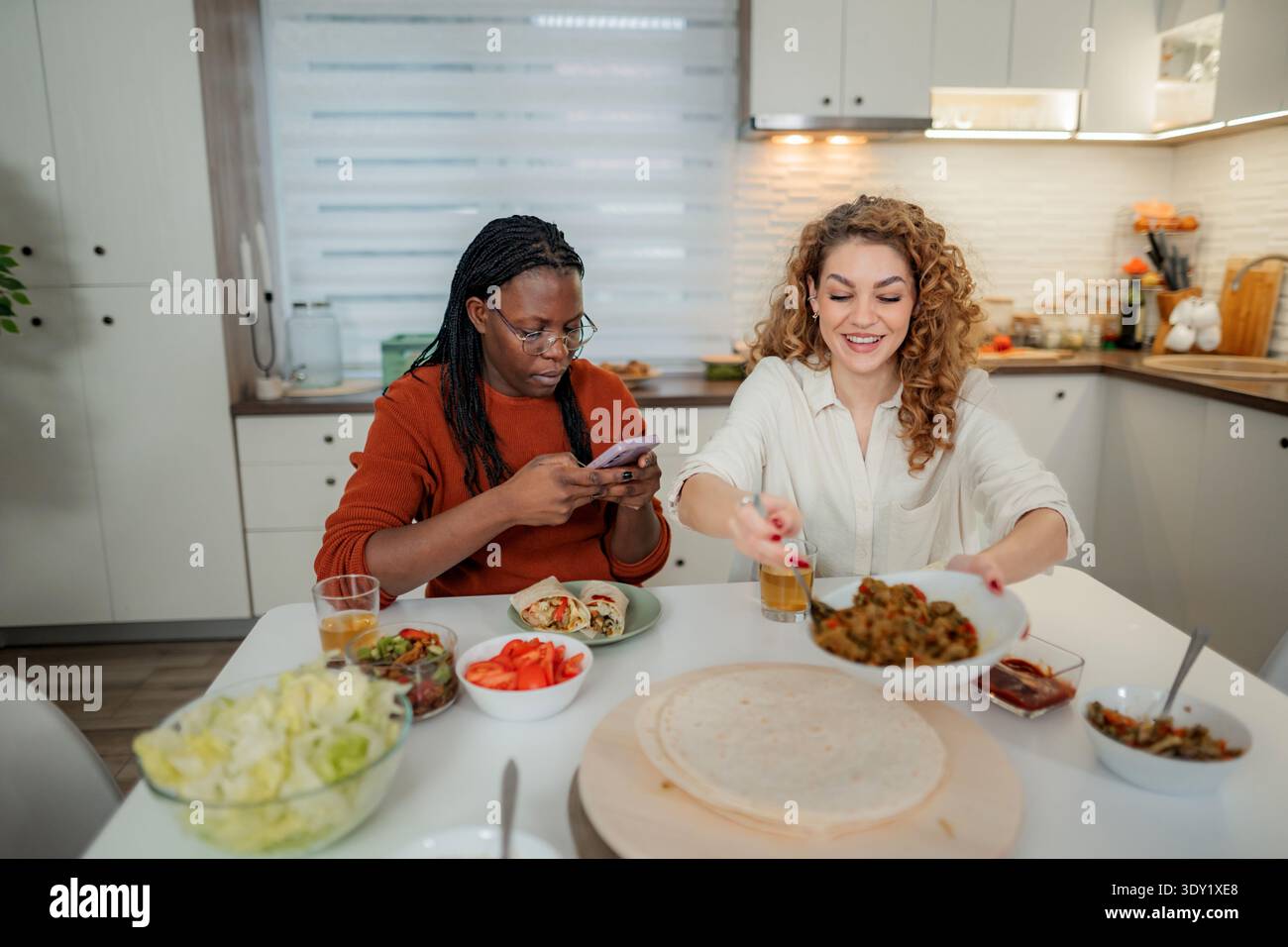Diverse friends preparing food and using phone in kitchen Stock Photo