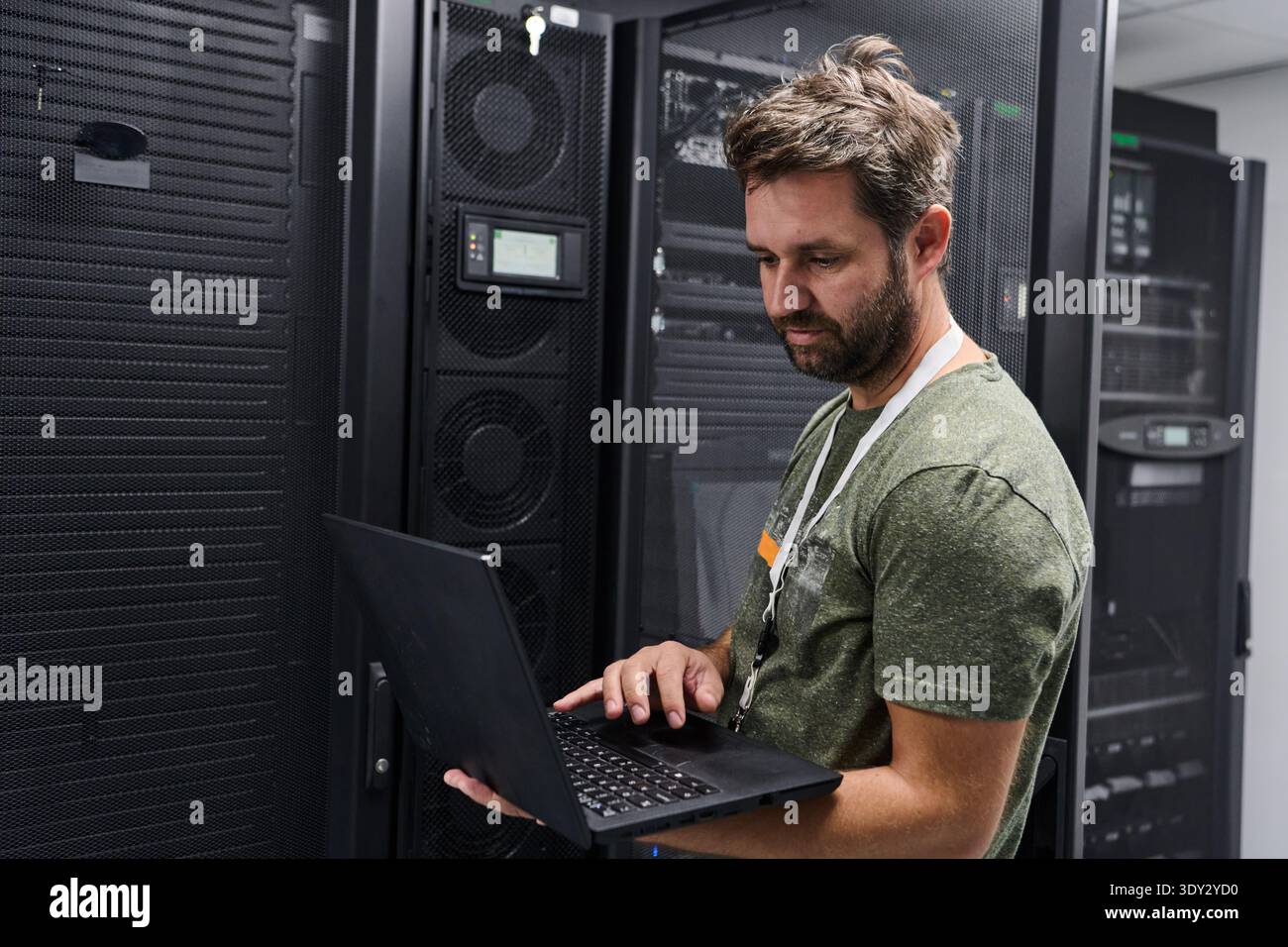 IT technician working on laptop in a data center server room checking network equipment Stock Photo