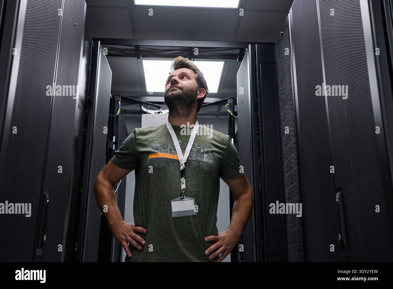 IT technician inspecting server racks in a data center under bright overhead lights Stock Photo