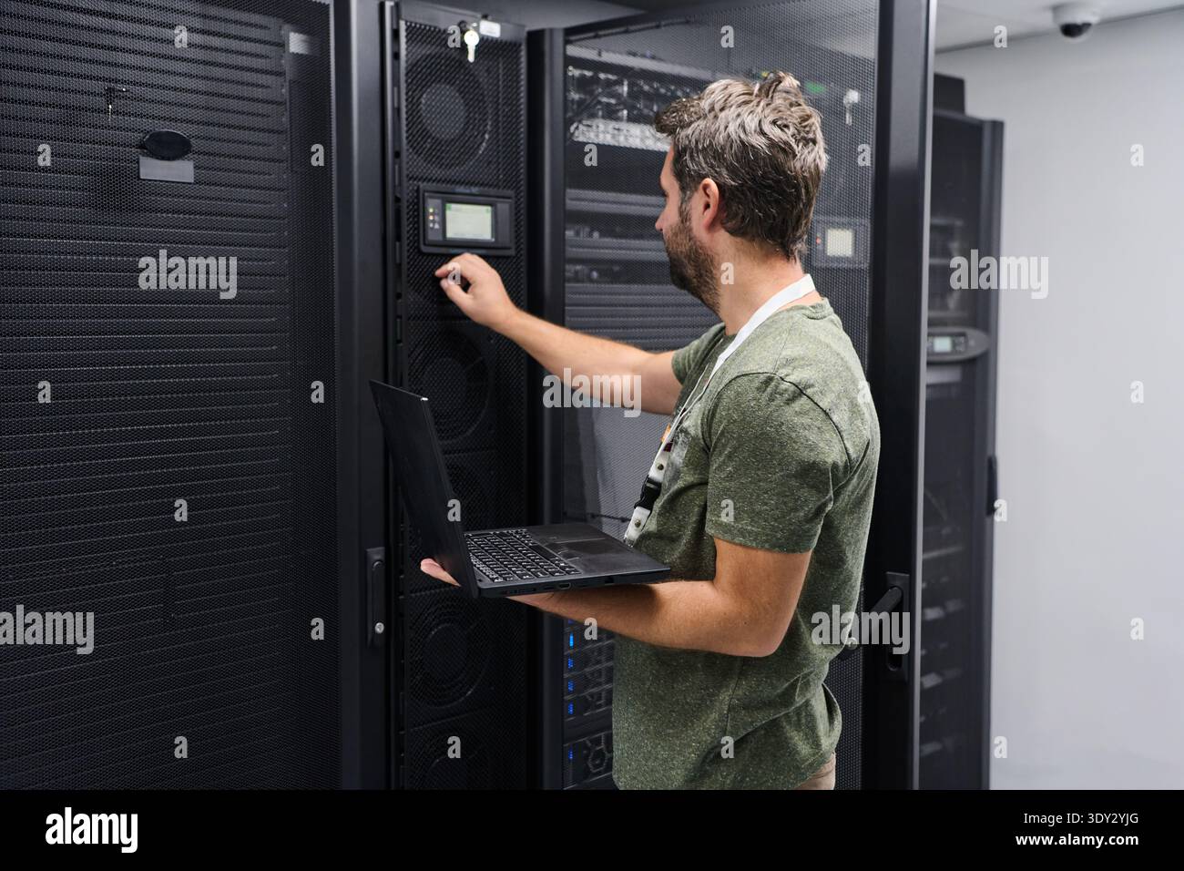 IT technician configuring server equipment in a data center while holding a laptop and checking network settings Stock Photo