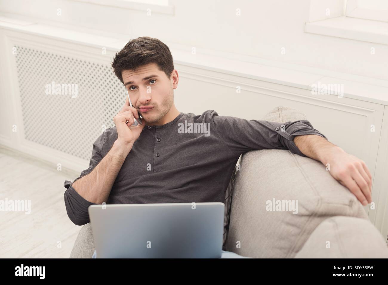 Serious young man at home with laptop and mobile Stock Photo